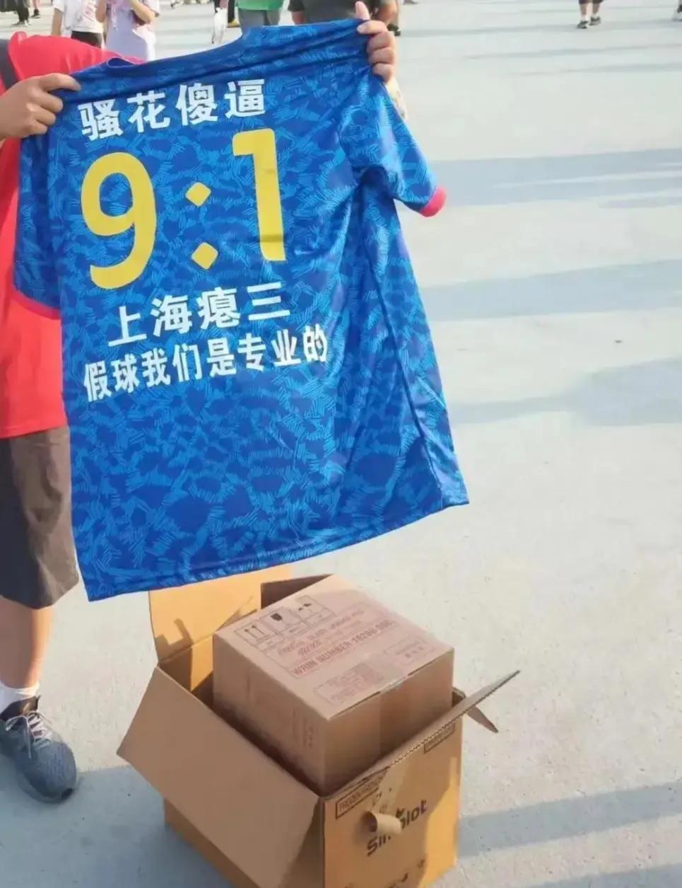 过分了！京沪大战前的工体门口，一名北京国安球迷举着一件印着“9-1”的球衣，上面