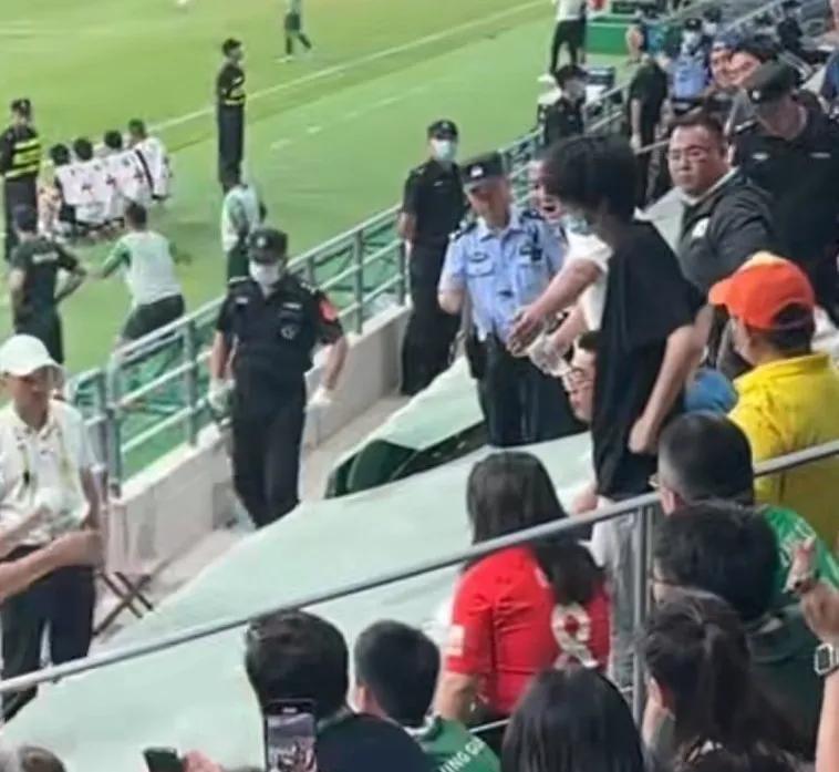 面对一个穿着上港队红色球衣的女子，一大群北京球迷群起而攻之，女球迷在安保人员的护(2)
